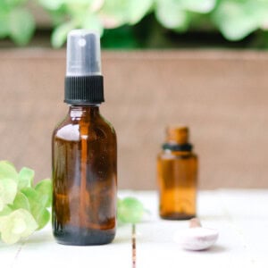 A bottle of homemade febreze and a bottle of essential oil on a white table.