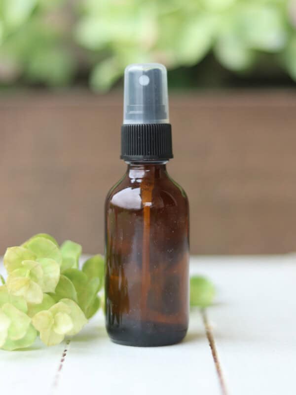 A bottle of homemade febreze on a white table with green flowers.
