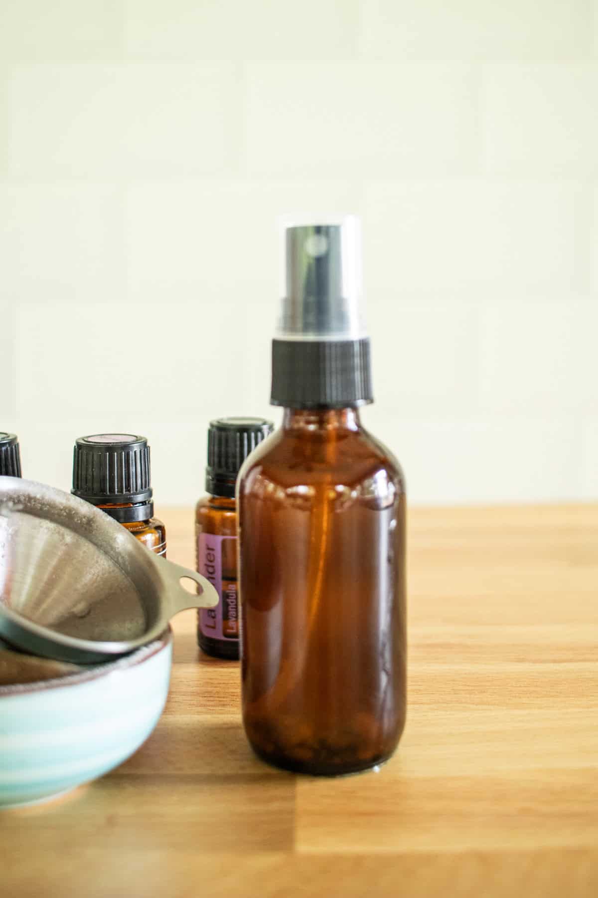 An amber spray bottle with essential oils and a funnel behind it.