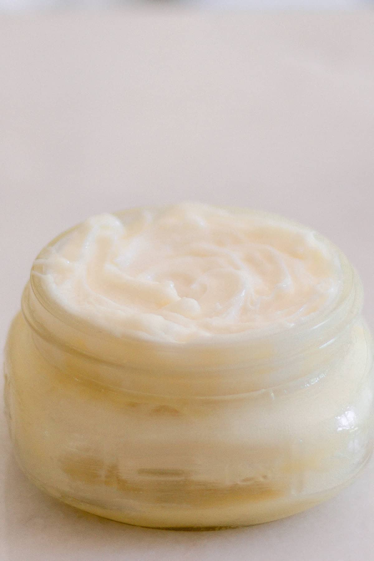 A jar of whipped mango body butter on a white countertop.