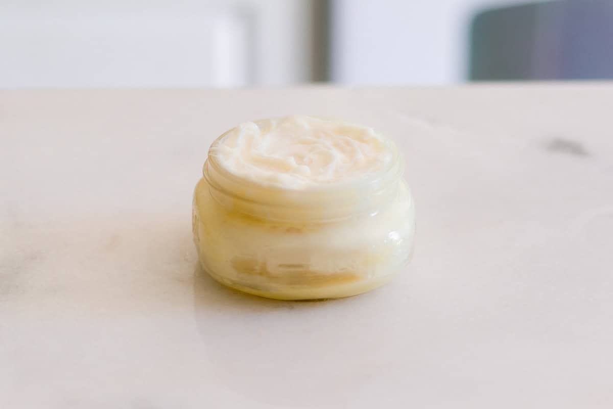 A jar of whipped mango body butter on a white counter.