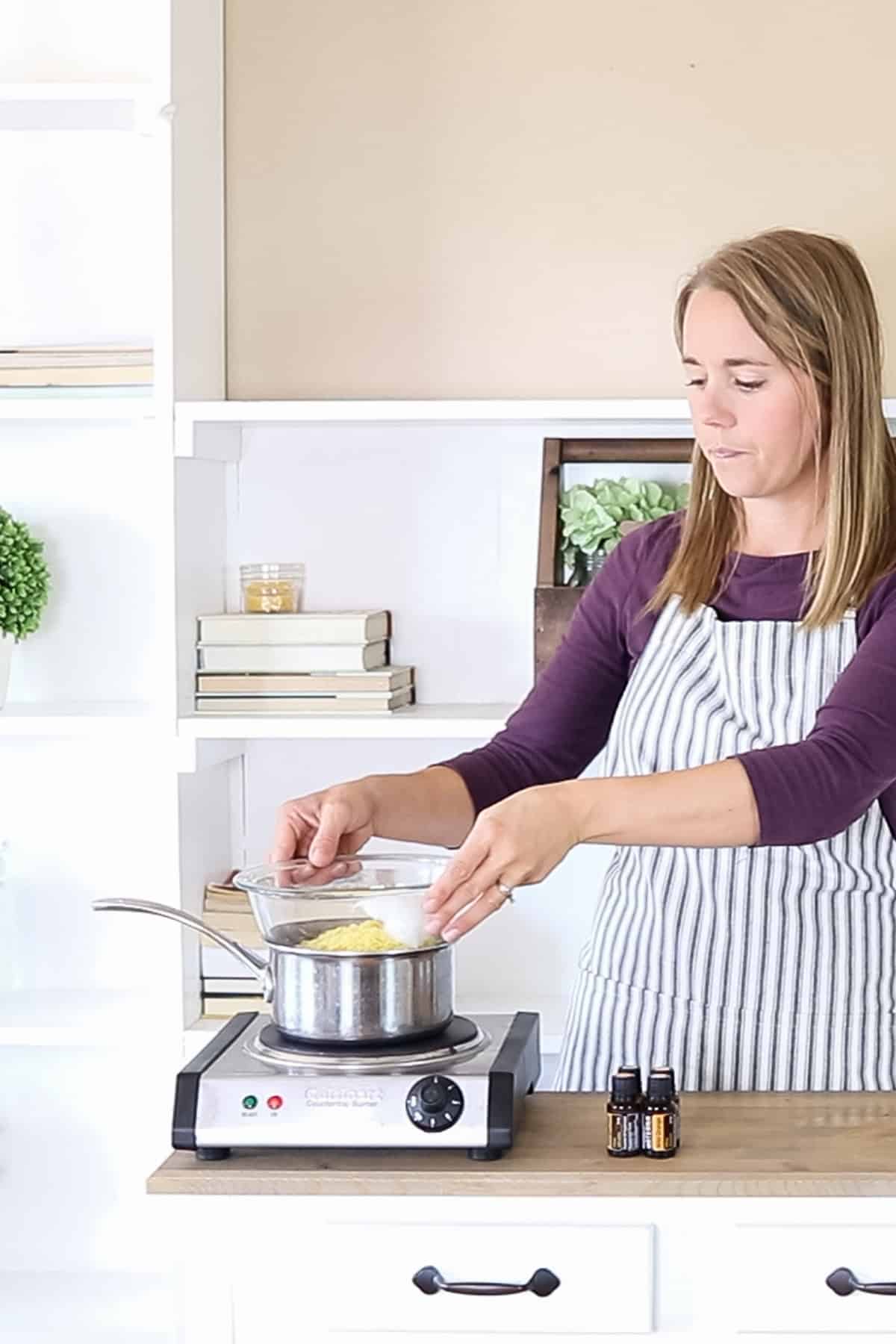 Laura placing a bowl of wax on top of a boiling pot of water to create a double boiler. 