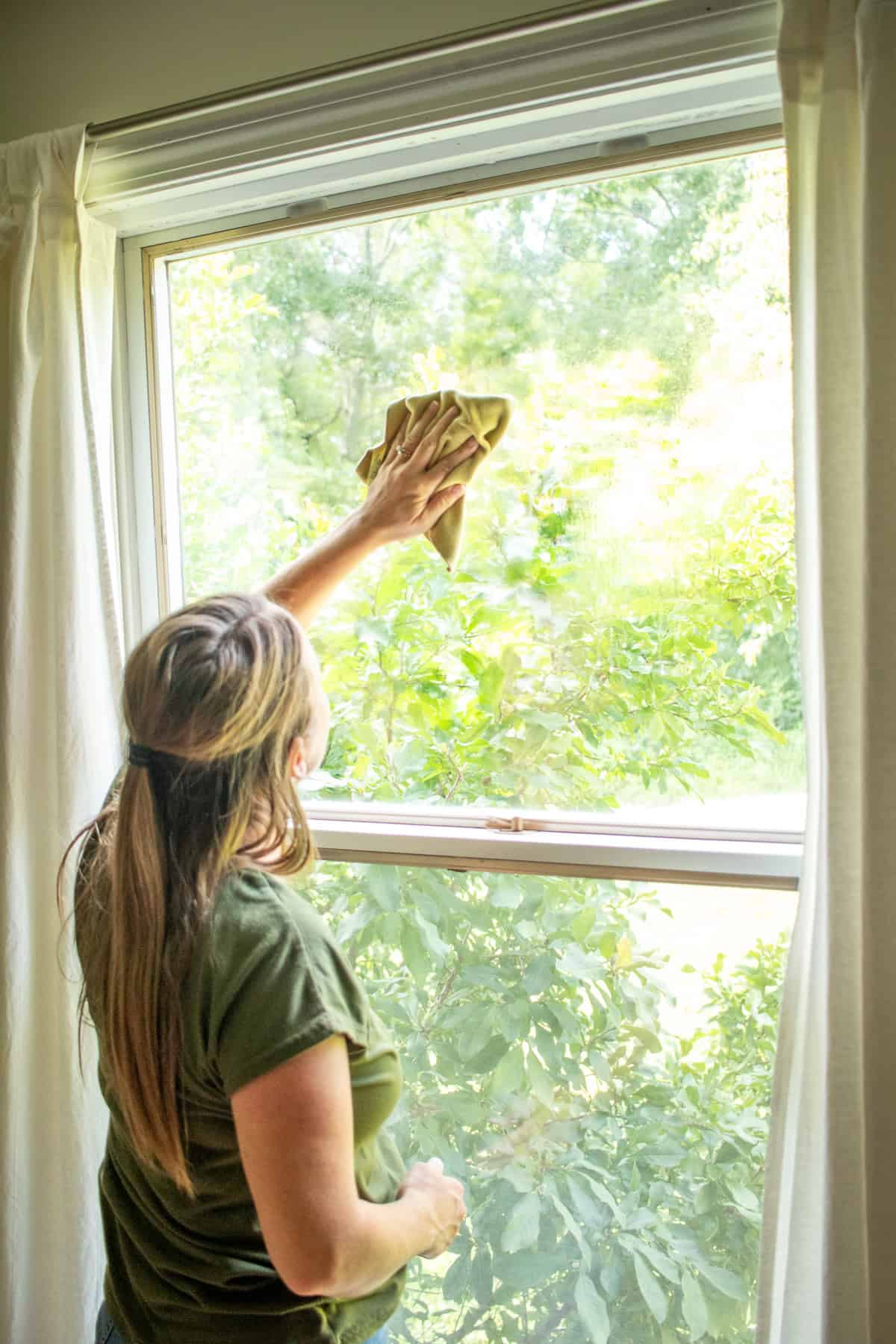 Wiping the window clean with a microfiber cloth after it has been sprayed with the cleaning solution.