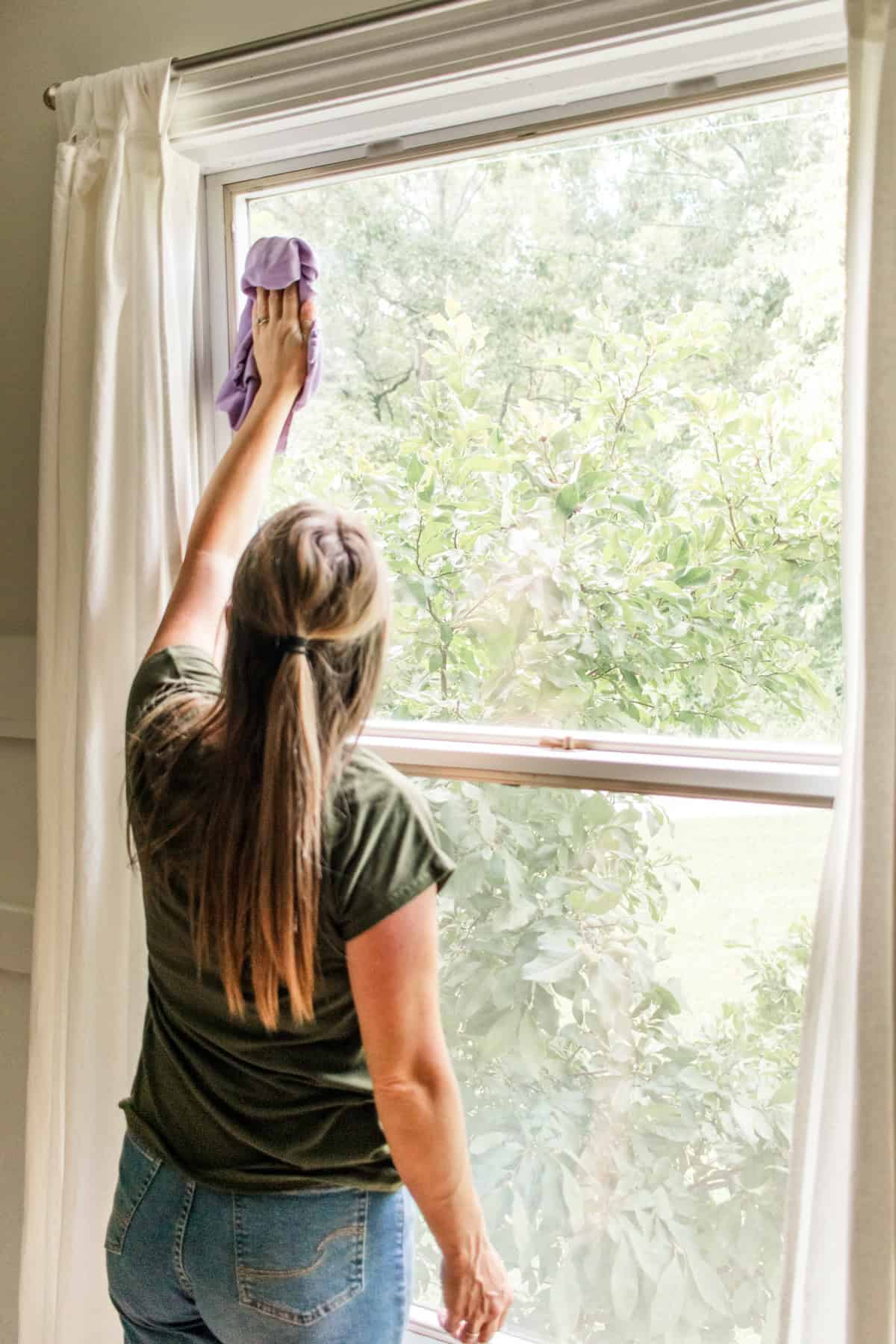 Wiping away cobwebs from the corners of the window with a clean, purple rag. 