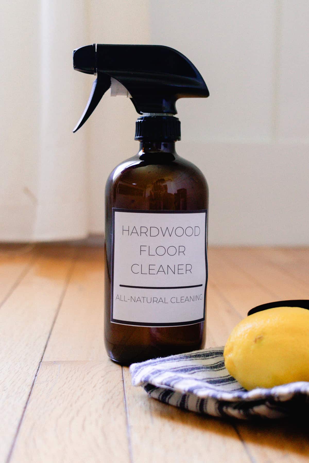 A spray bottle of wood floor cleaner with a lemon and a towel.