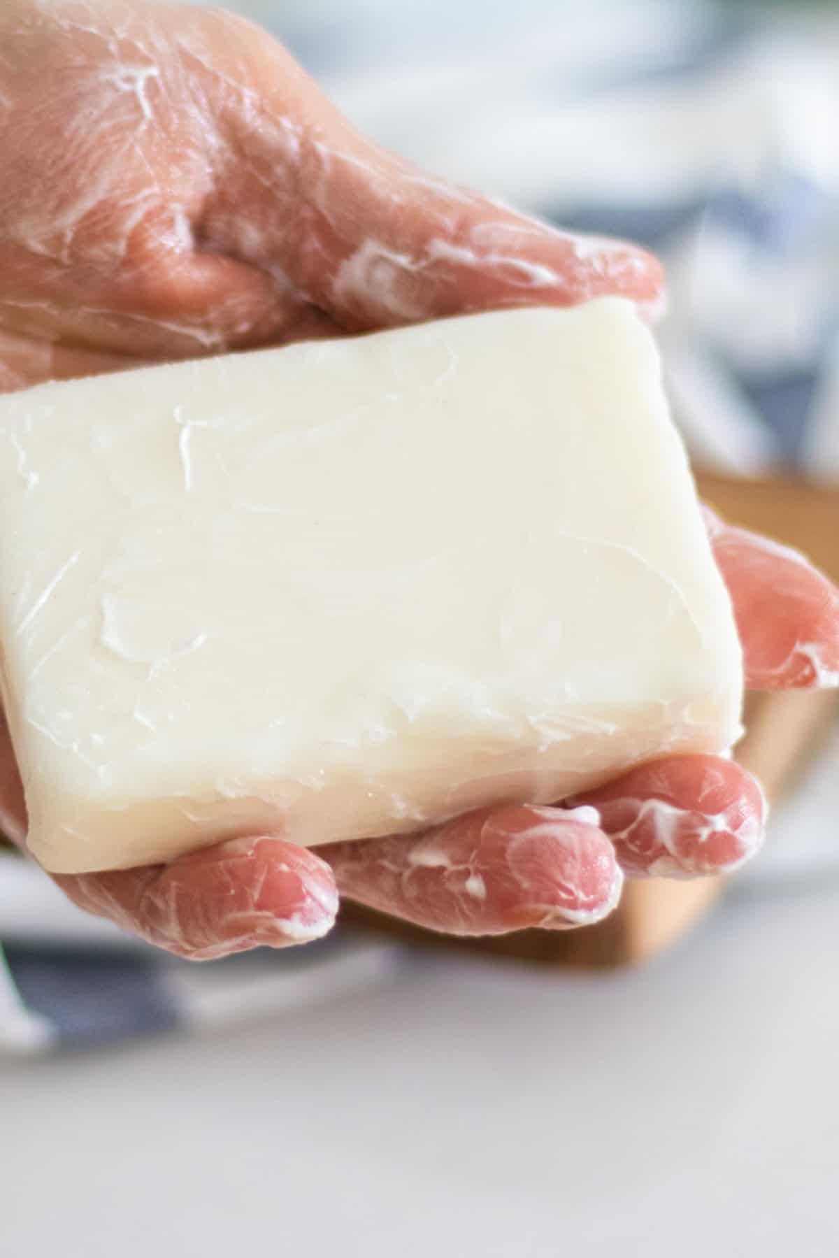 A hand holding a bar of cold process tallow soap.