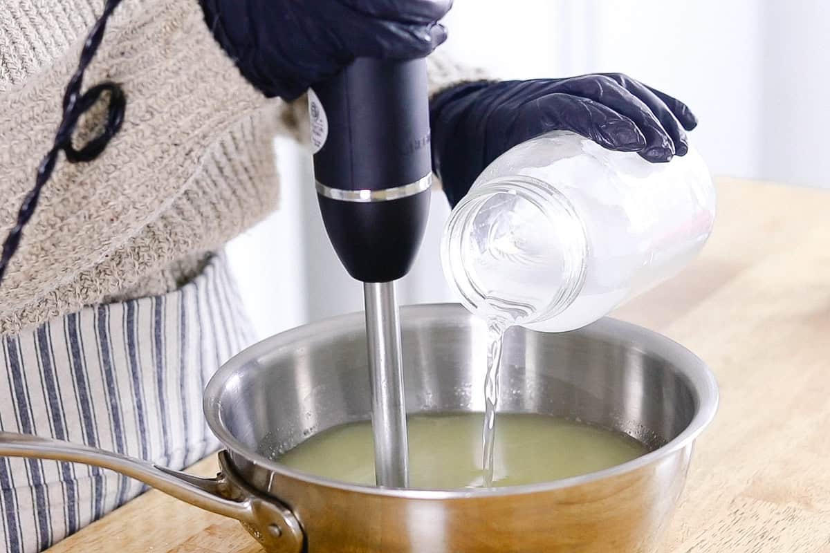 Pouring lye and water mixture into a bowl of melted tallow with an immersion blender.