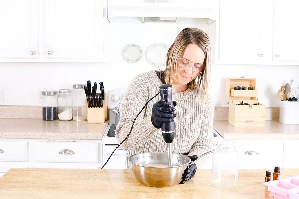 Blending a metal bowl of soap mixture with an immersion blender.