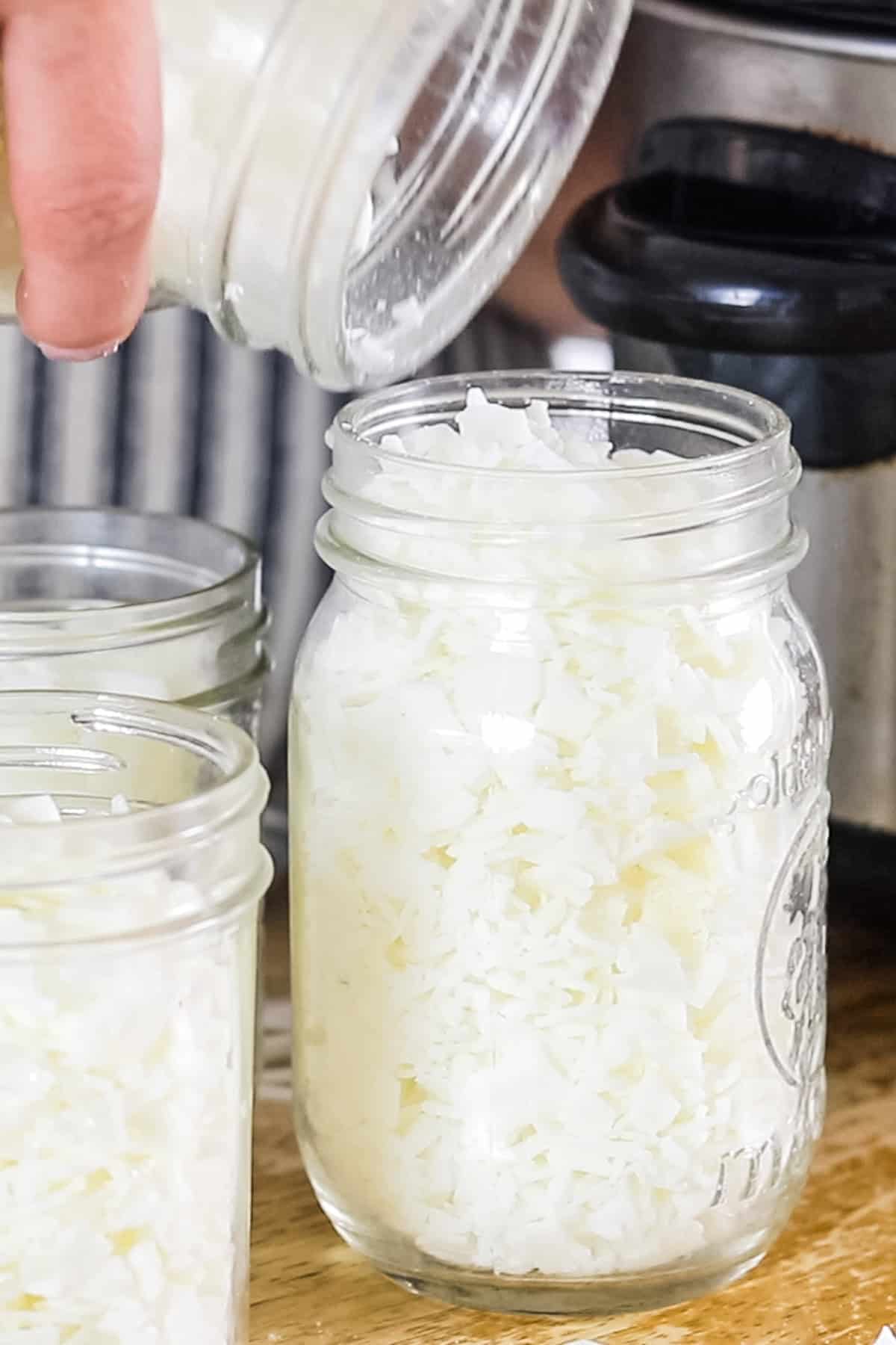 Pouring wax pellets into a mason jar.