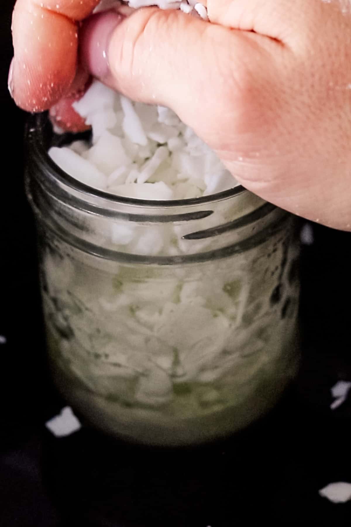 Adding more wax pellets to a jar of partially melted wax.