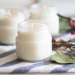 Three homemade Christmas candles with greenery and berries in the background.