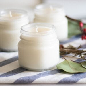 Three homemade Christmas candles with greenery and berries in the background.