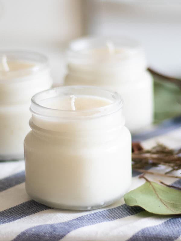 Three homemade Christmas candles with greenery on a white and blue towel.