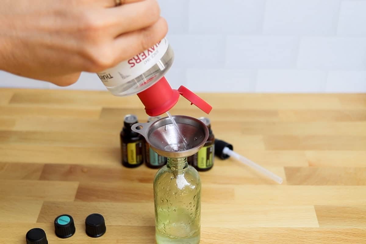 Pouring witch hazel into the spray bottle with a metal funnel.