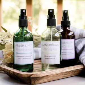 Homemade linen sprays scented with essential oils on a wooden tray with homemade labels.