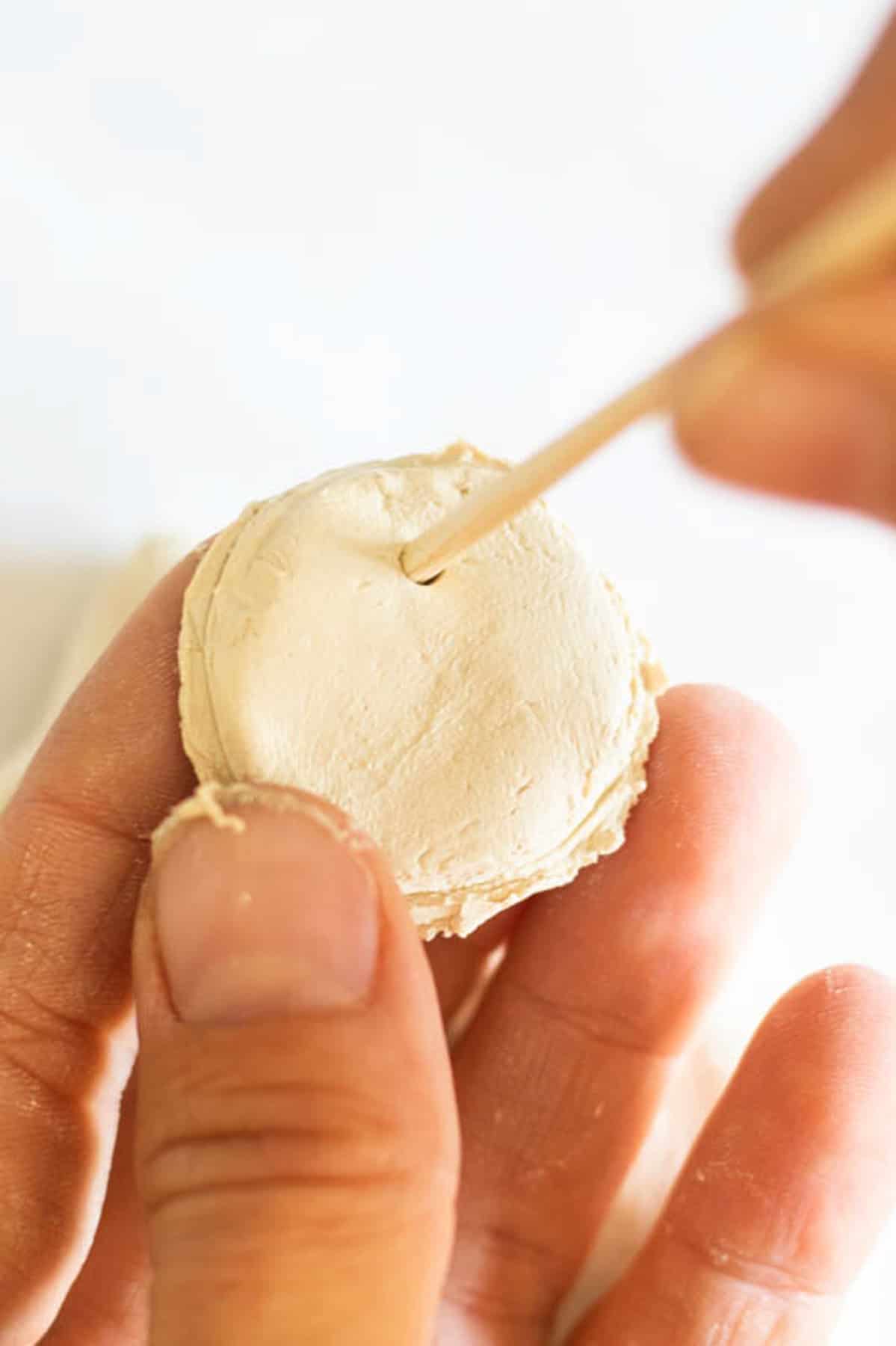 Poking a hole in a clay circle with a bamboo skewer.