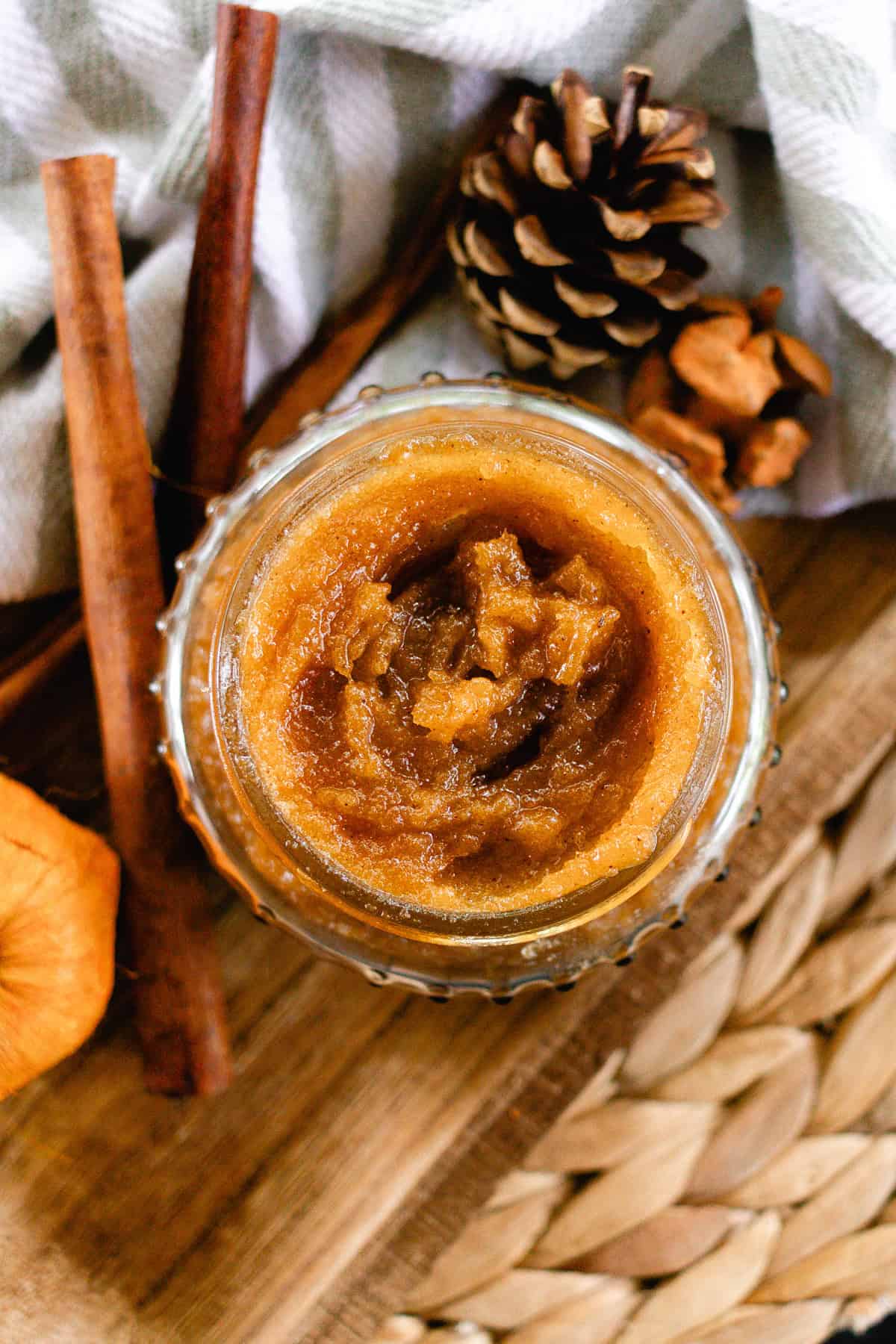 A jar of pumpkin spice body scrub with pinecones and cinnamon sticks.
