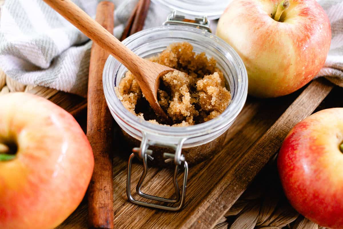 A jar of fall body scrub with fresh apple with cinnamon sticks.
