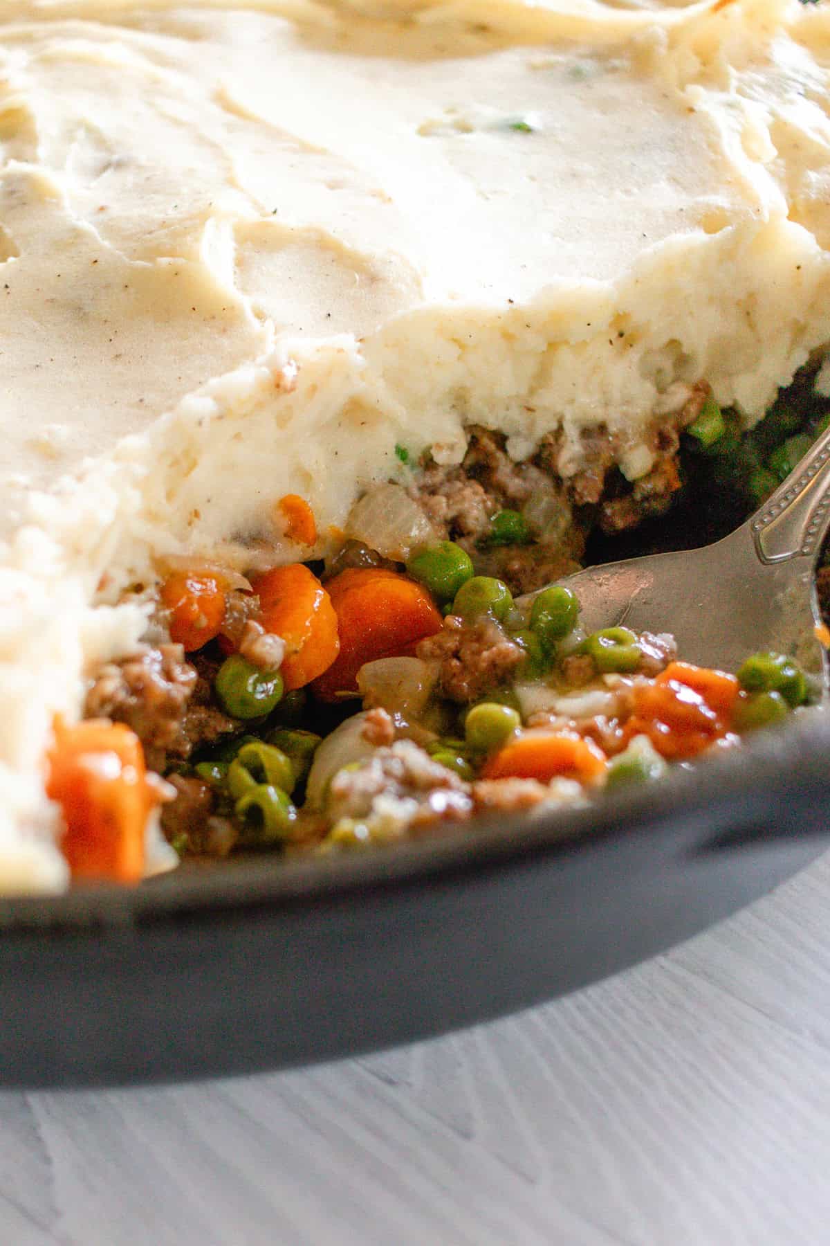 A close-up of a gluten-free shepherd's pie being scooped out of a cast iron skillet.