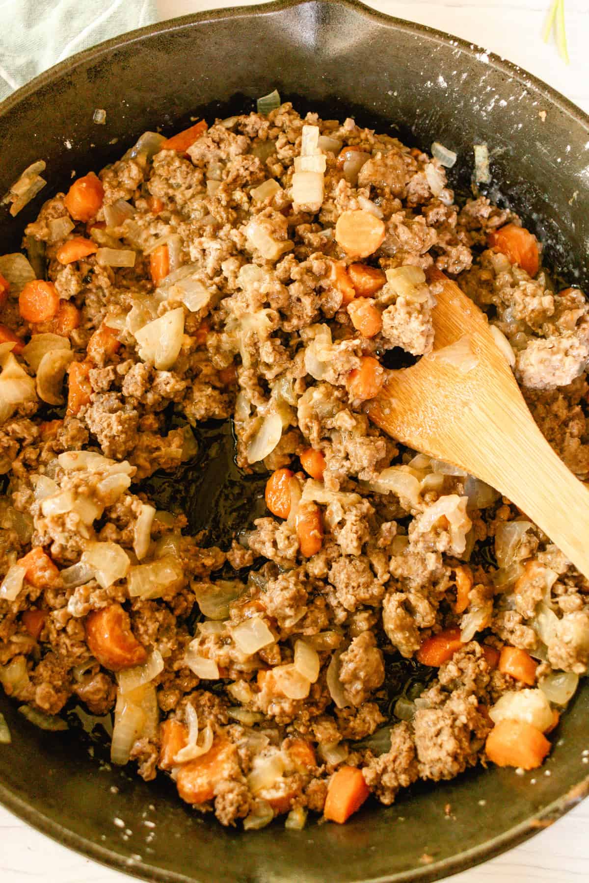 Cooking beef and carrots with beef broth in a cast iron skillet.