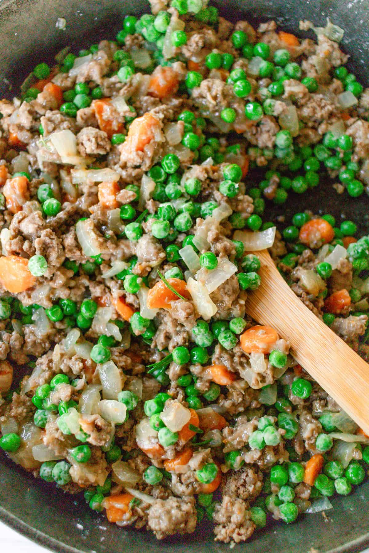 Stirring peas into shepherd's pie filling in a cast iron skillet.