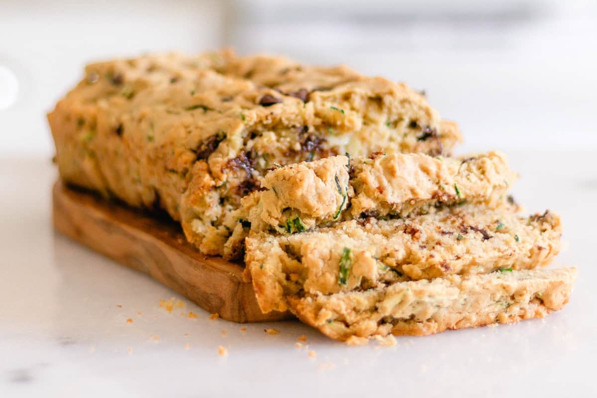 A loaf of gluten-free zucchini bread sliced on a wooden board.