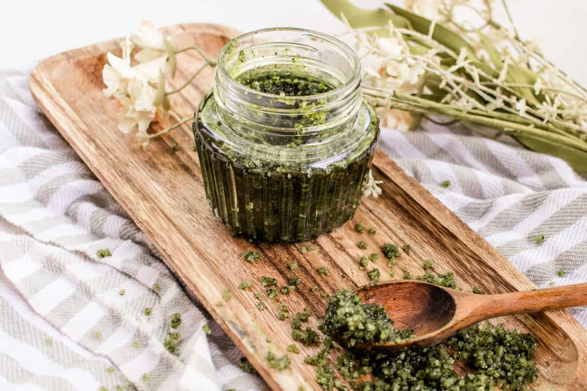 Green tea matcha scrub in a jar on a wooden board with a spoon.