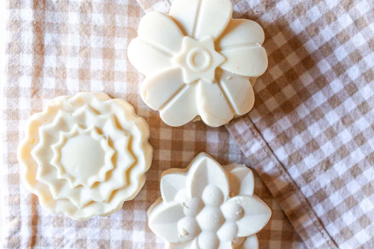 Three flower-shaped bars of lard soap on a gingham print towel.