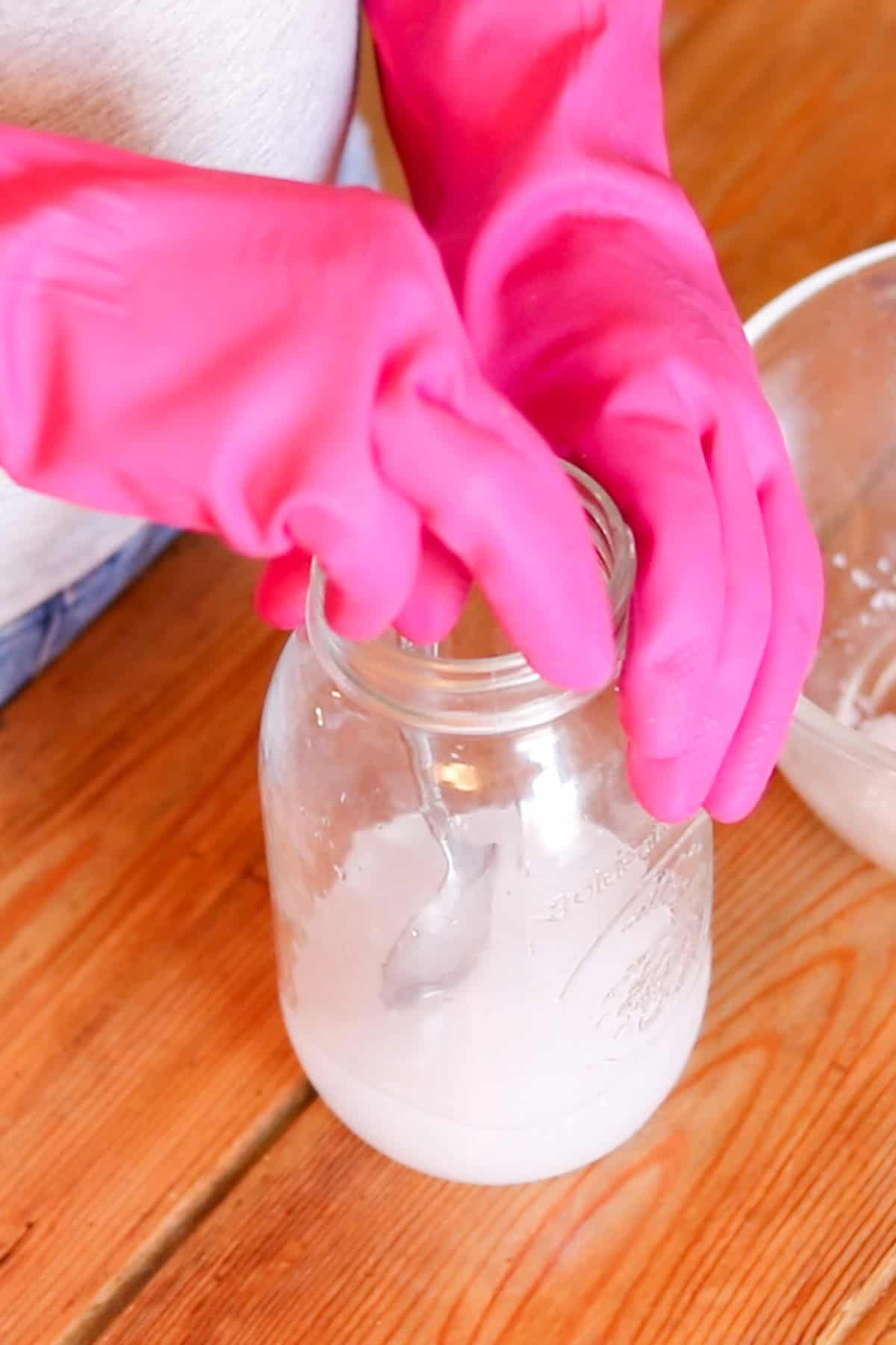 Mixing lye and water in a glass jar with rubber gloves on.