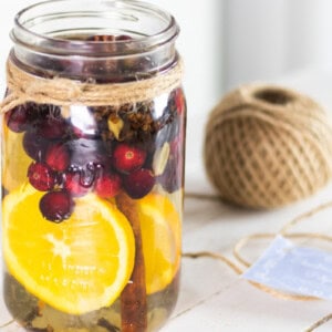 Stovetop potpourri in a glass jar with sliced oranges and fresh cranberries.
