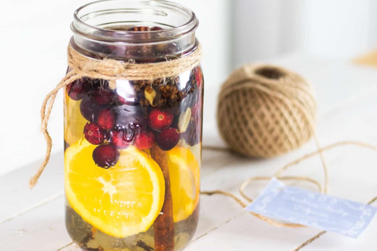 Stovetop potpourri in a glass jar with sliced oranges and fresh cranberries.