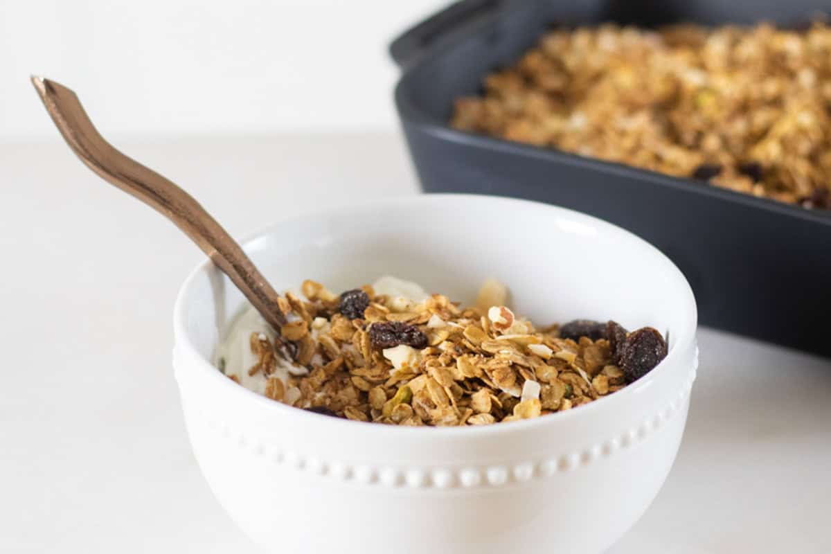 A white bowl of honey granola with a spoon sticking out of it.