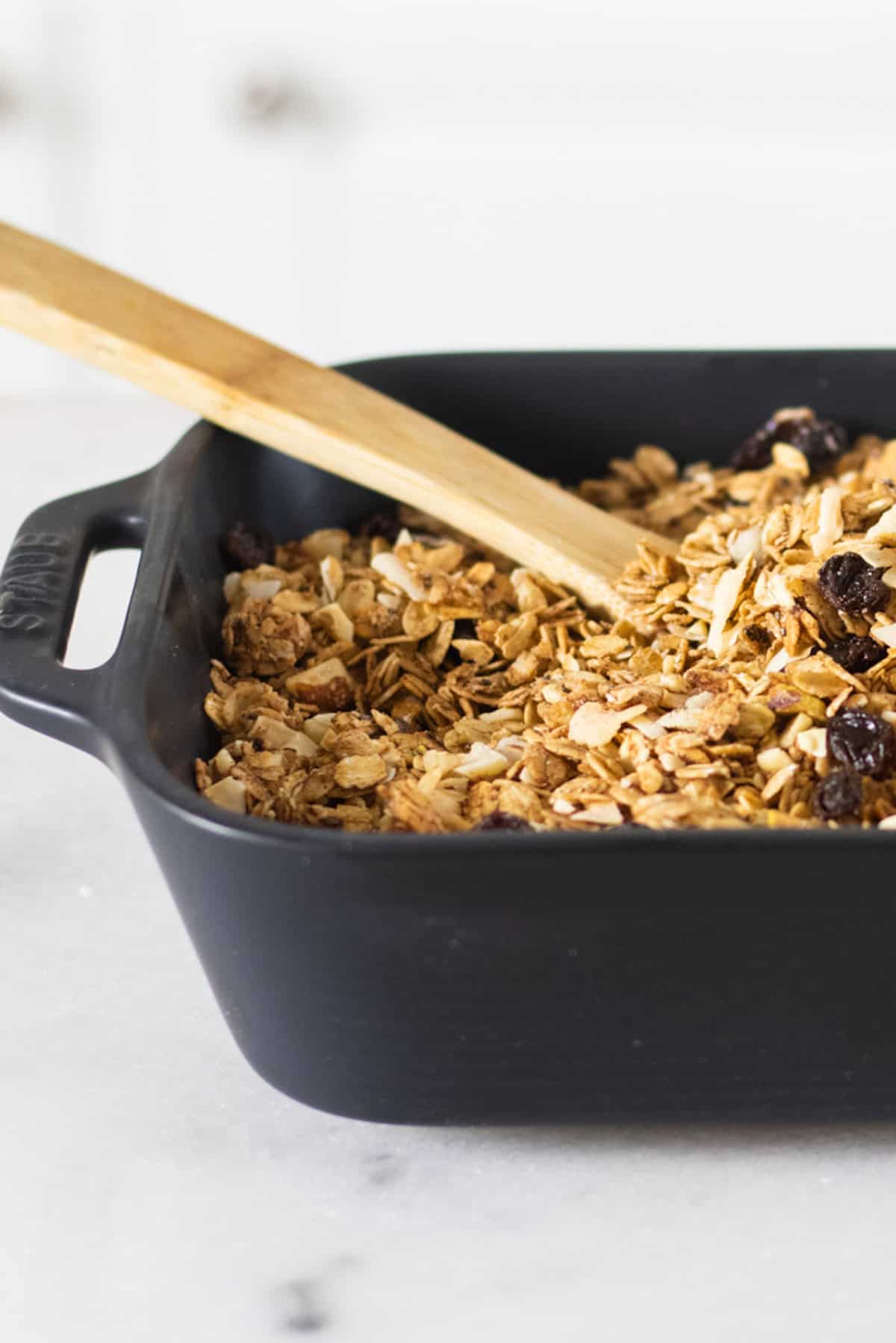 A baking dish filled with honey granola with a wooden spoon in it.