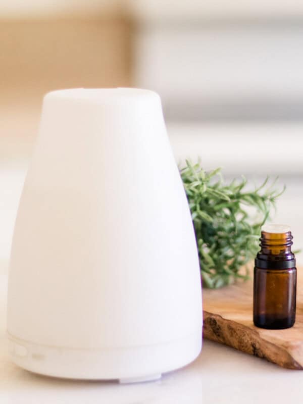 A diffuser on a white table with a bottle of essential oil.
