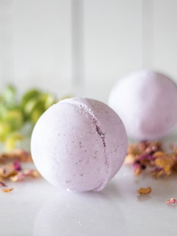 Two purple bath bombs with dried flowers and greenery.