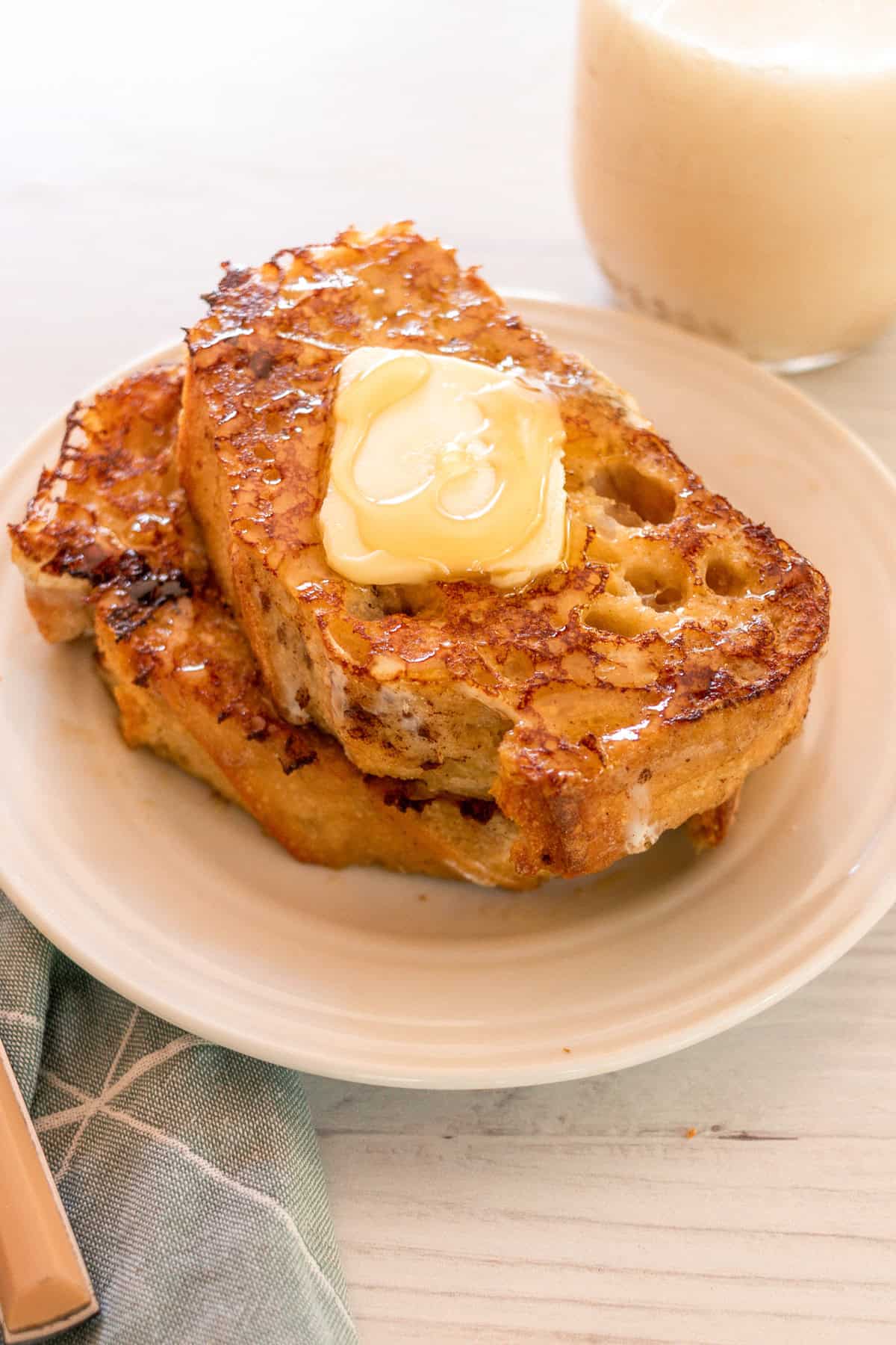 A white plate with a stack of sourdough french toast and butter.