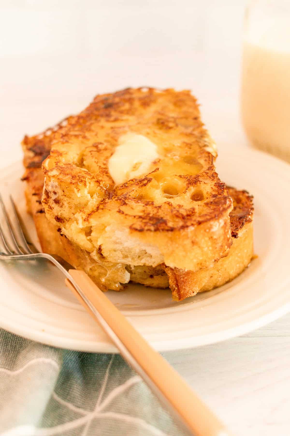 A white plate with a fork and sourdough french toast with butter.