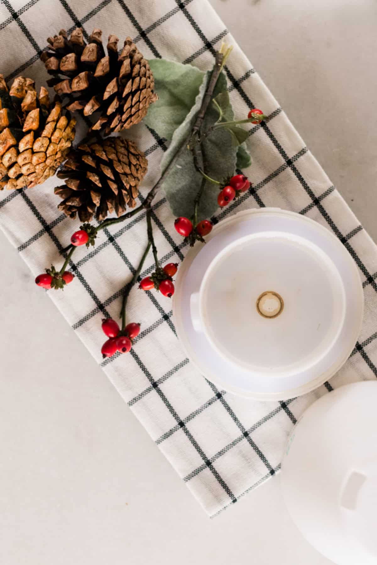 Looking down on a diffuser, red berries, and pinecones on a plaid towel.