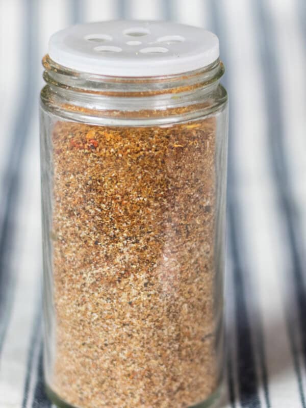 A jar of homemade gluten-free taco seasoning on a striped tablecloth.