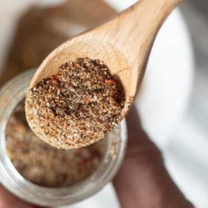 A wooden measuring spoon scooping homemade taco seasoning out of a jar.