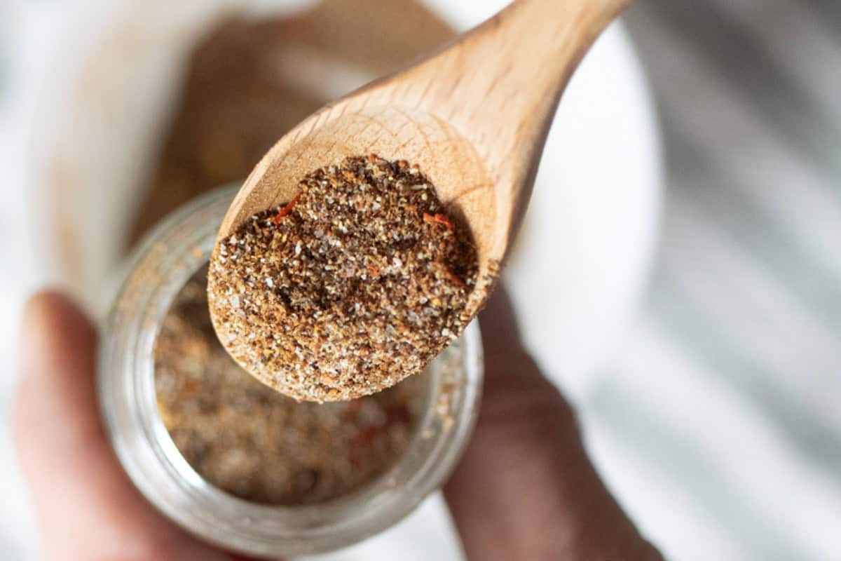 A wooden measuring spoon scooping homemade taco seasoning out of a jar.