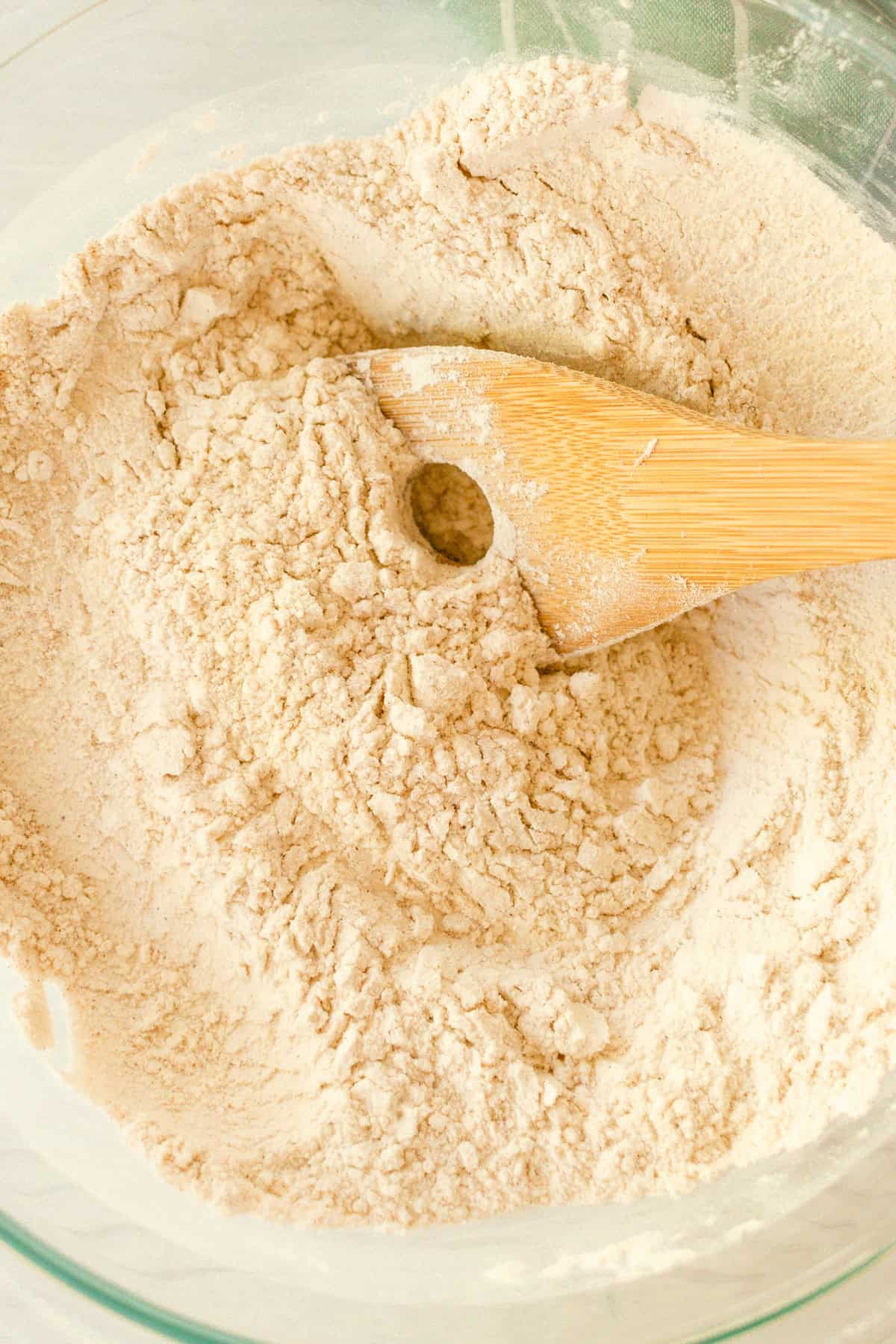 Dry ingredients combined in a clear mixing bowl with a wooden spatula. 