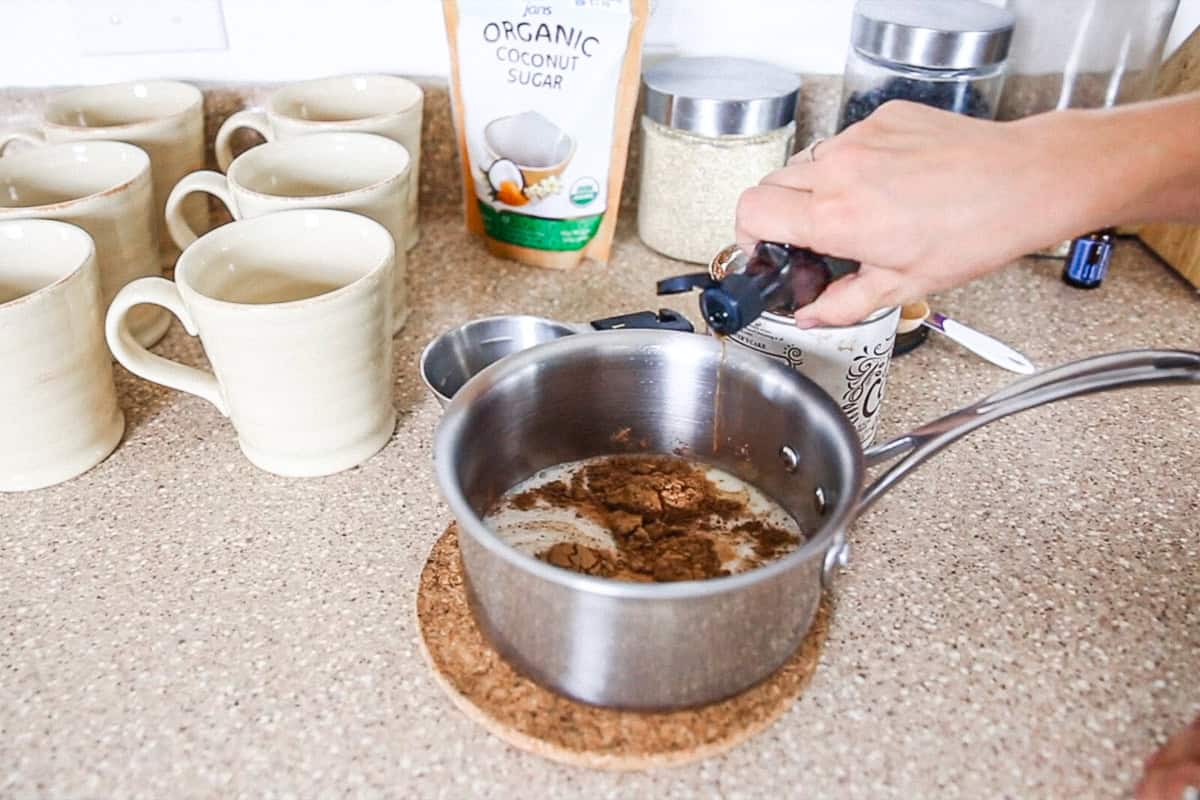 Dropping peppermint extract into a pot of paleo hot cocoa.