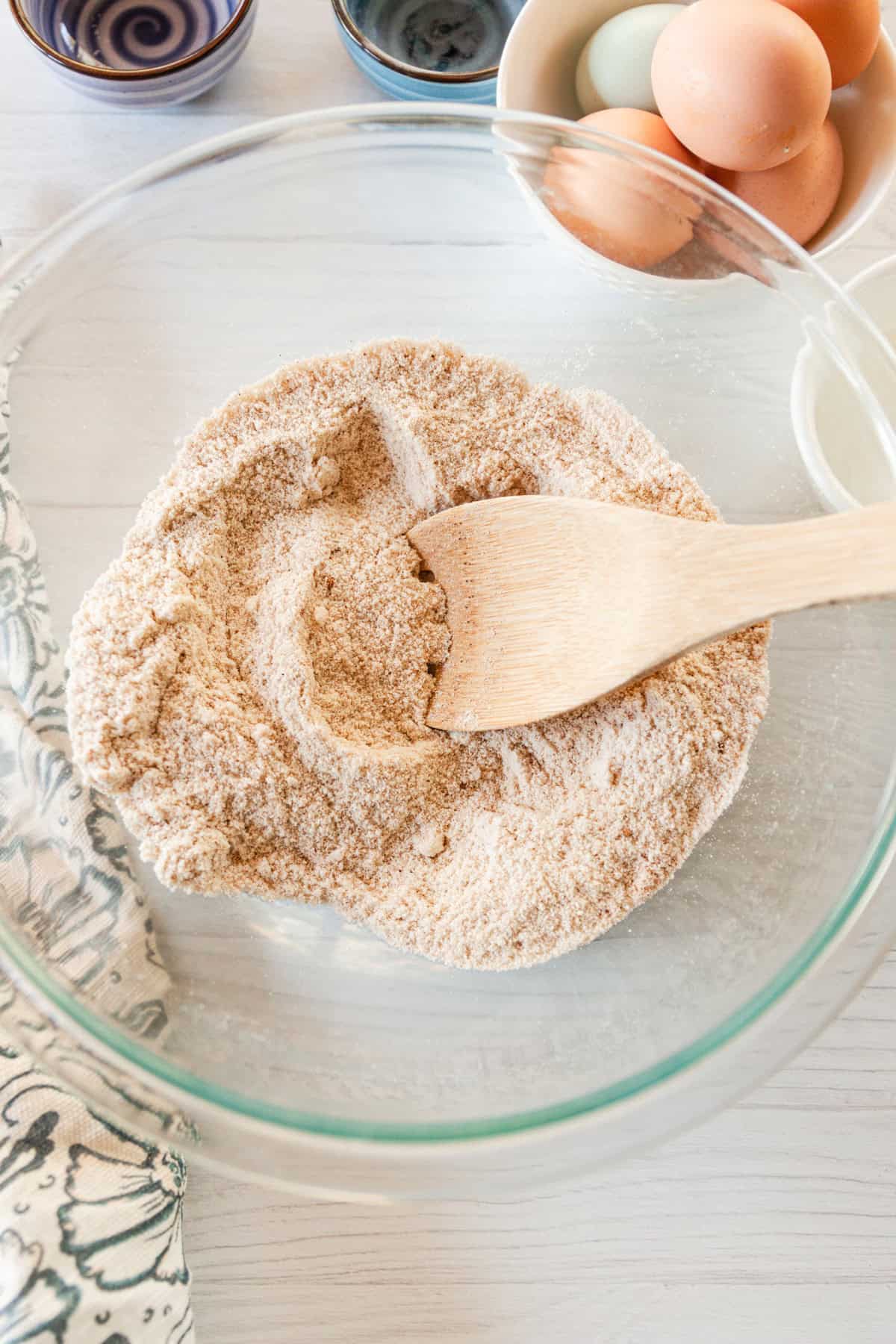 Using a wooden spoon to combine the dry ingredients in a clear mixing bowl. 