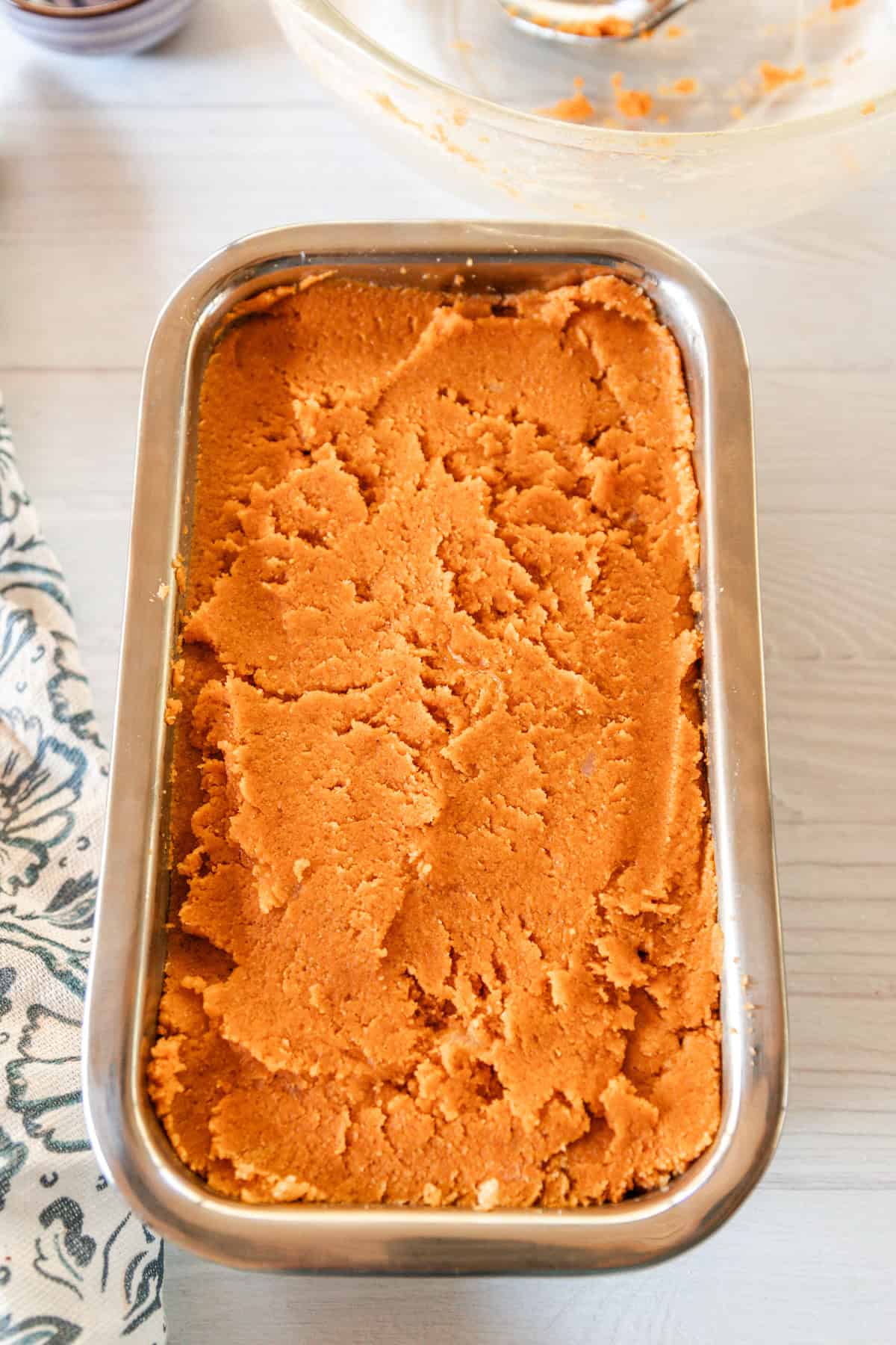 The batter for the paleo pumpkin bread spread evenly in a small loaf pan on a wooden table.