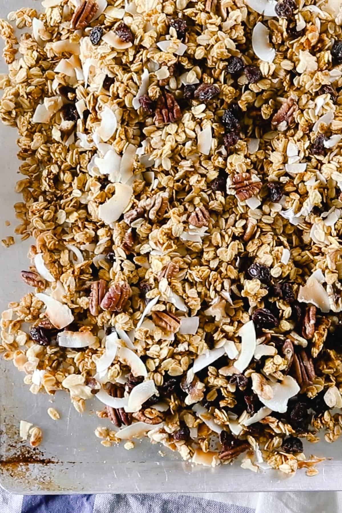Adding the nuts and fruit to a sheet pan of granola.
