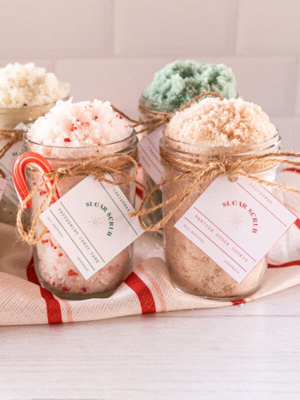 5 jars with homemade christmas scrubs on a red striped towel.