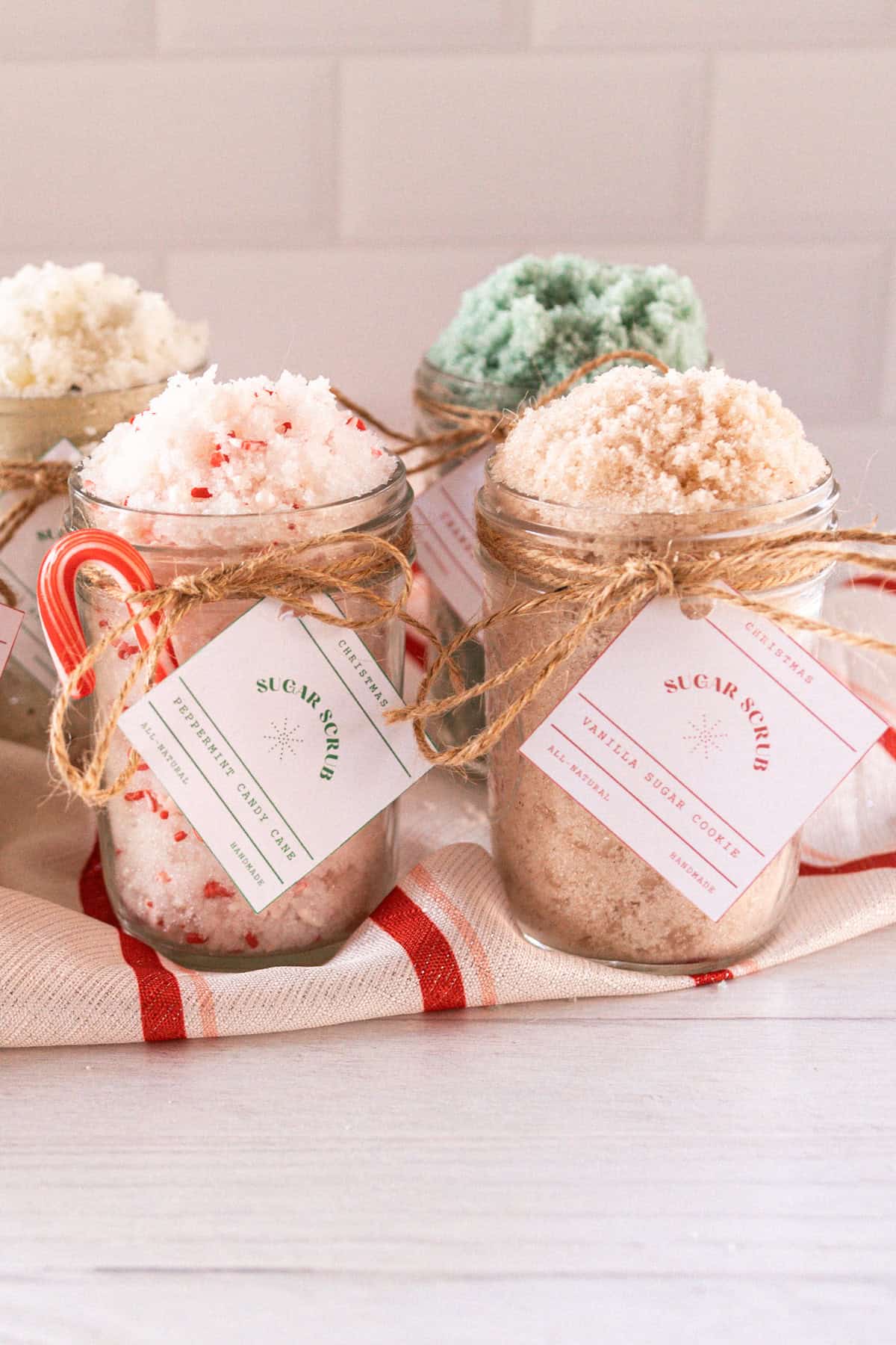 5 jars with homemade christmas scrubs on a red striped towel.