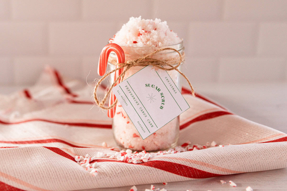 A jar of candy cane sugar scrub on a red and white towel with a candy cane and label tied to the jar. 