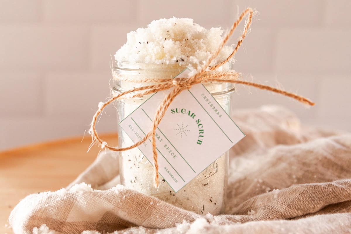 A jar of chai spice sugar scrub with a label tied on with twine and a beige towel.